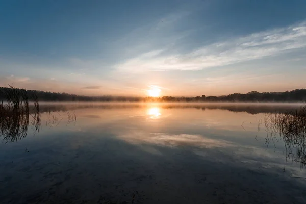 Beautiful, red dawn on the lake. The rays of the sun through the fog. The blue sky over the lake, the morning comes, the forest is reflected in the water.