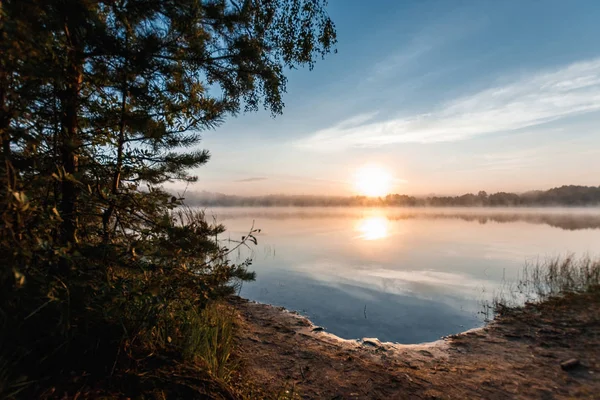 Beautiful, red dawn on the lake. The rays of the sun through the fog. The blue sky over the lake, the morning comes, the forest is reflected in the water.