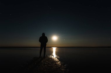 Parlak yıldız ve süt ile yıldızlı gökyüzü altında ay batımında adam sahanın yolu. Yıldızlı gece gökyüzü kontrast fotoğraf. Ay su ışınlarından yansıması.