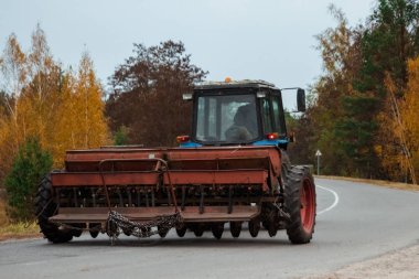 Bir buğday alanında bir yol boyunca tarım işleri için bir römork ile mavi bir traktör sürmek.