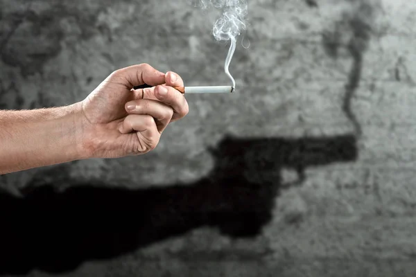 Mano masculina sosteniendo un cigarrillo, sombra en la pared con un arma, primer plano, fondo claro. Fondo creativo. El concepto de fumar mata, nekatin es veneno, adicción a la nicotina. Copiar espacio . — Foto de Stock
