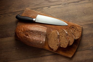 Ahşap kesme tahtası üzerinde düz dilimlenmiş çavdar ekmeği ve bir bıçak yakın çekim yaratıcı arka plan yattı, kopya alanı. Taze pasta, siyah ekmek kavramı.