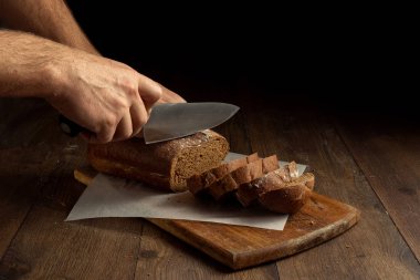 Yaratıcı arka plan, bir ahşap kesme tahtası üzerinde düz yatıyordu, kopya alanı çavdar ekmeği yakın çekim, erkek ellerini kesti. Taze pasta, siyah ekmek kavramı.
