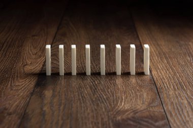 Yaratıcı arka plan, beyaz domino, kahverengi ahşap arka plan üzerinde. Domino etkisi kavramı, zincirleme reaksiyon, risk yönetimi, kopyalama alanı.