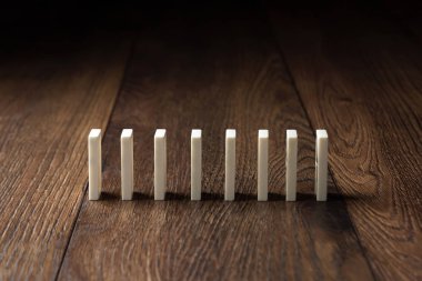 Yaratıcı arka plan, beyaz domino, kahverengi ahşap arka plan üzerinde. Domino etkisi kavramı, zincirleme reaksiyon, risk yönetimi, kopyalama alanı.