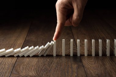 Yaratıcı arka plan, Erkek eli domino etkisi durdu, kahverengi ahşap arka plan üzerinde. Domino etkisi kavramı, zincirleme reaksiyon, risk yönetimi, kopyalama alanı.
