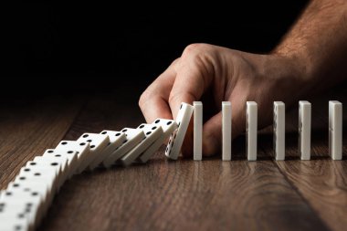 Yaratıcı arka plan, Erkek eli domino etkisi durdu, kahverengi ahşap arka plan üzerinde. Domino etkisi kavramı, zincirleme reaksiyon, risk yönetimi, kopyalama alanı.
