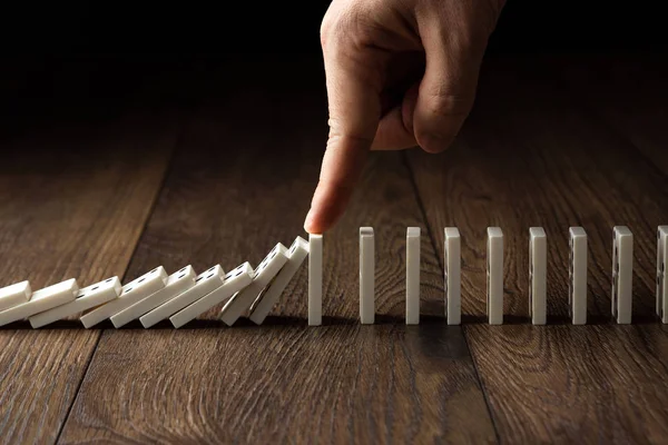 Creative background, Men's hand stopped domino effect, on a brown wooden background. Concept of domino effect, chain reaction, risk management, copy space.