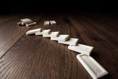 Yaratıcı arka plan, beyaz domino, kahverengi ahşap arka plan üzerinde. Domino etkisi kavramı, zincirleme reaksiyon, risk yönetimi, kopyalama alanı.
