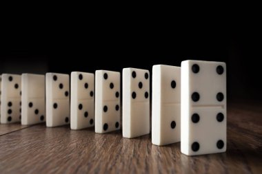 Yaratıcı arka plan, beyaz domino, kahverengi ahşap arka plan üzerinde. Domino etkisi kavramı, zincirleme reaksiyon, risk yönetimi, kopyalama alanı.