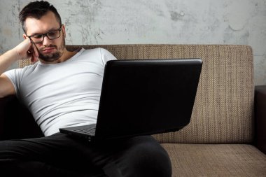 Kanepede oturan beyaz gömlekli adam, iş yerinde dizüstü bilgisayarda uyuyakalmış. Tembellik kavramı, ilgisizlik, hayal kırıklığı, erteleme, evde kişi. kopyalama alanı.