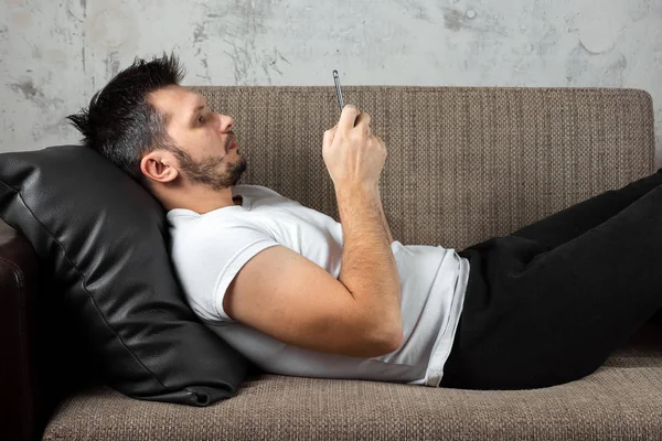 The guy in the white shirt is lying on the couch and sitting in the phone. The concept of laziness, apathy, frustration, procrastination, the person at home. copy space.