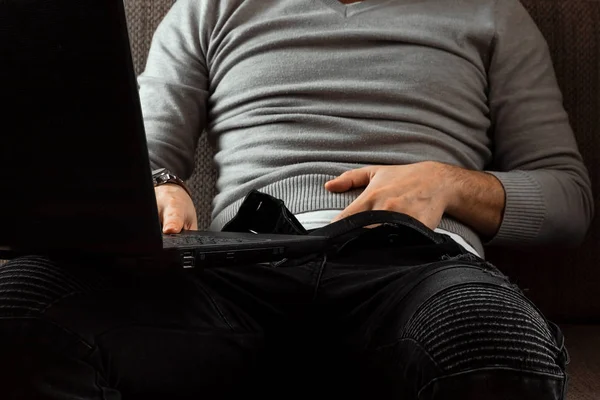 A man watches an adult video on a laptop while sitting on the couch. The concept of porn, men\'s needs, pervert, lust, desire, loneliness.