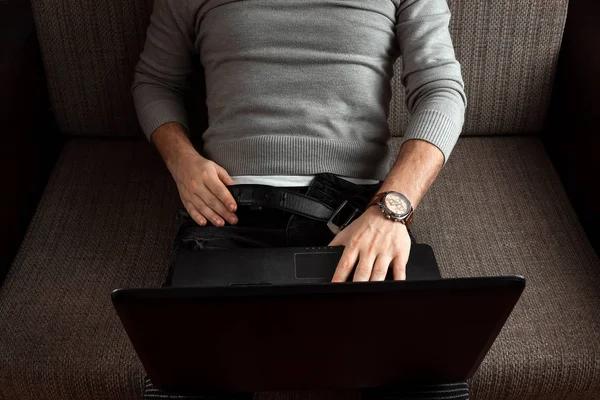 A man watches an adult video on a laptop while sitting on the couch. The concept of porn, masturbation, male needs, pervert, lust, desire, loneliness.