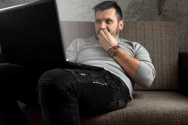 A man watches an adult video on a laptop while sitting on the couch. The concept of porn, men\'s needs, pervert, lust, desire, loneliness.