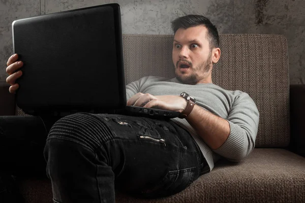 A man watches an adult video on a laptop while sitting on the couch. The concept of porn, masturbation, male needs, pervert, lust, desire, loneliness.