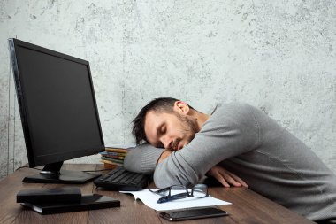 Bir adam, ofiste bir masada oturan bir adam ve değil çalışma, yorgun bir görünüm. Ofis işleri, tembellik, yorgunluk kavramı. Kopya alanı.