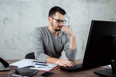 Bir bilgisayarda çalışan bir erkeğin, ofiste, bir masada oturan bir adam. Ofis işleri kavramı. Kopya alanı.