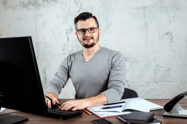 Bir bilgisayarda çalışan bir erkeğin, ofiste, bir masada oturan bir adam. Ofis işleri kavramı. Kopya alanı.