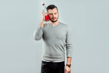 Bir kalıntı ve detoks kavramı. Alkol kafasına bir şişe tutan bir baş ağrısı olan bir adam. Stüdyo ışık arka plan