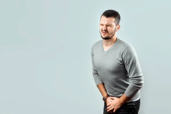 A young, attractive man feels pain in his groin, arms folded between his legs. Experiencing pain, male problems, potency. — Stock Image Young Attractive Man Feels Pain His Groin Arms Folded His Stock Photo