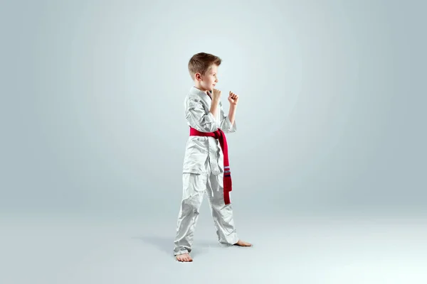 Creative background, a child in a white kimono in a fighting stance, on a light background. The concept of martial arts, karate, sports since childhood, discipline, first place, victory. copy space.