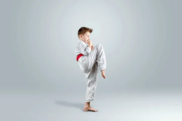 Creative background, a child in a white kimono makes a kick, on a light background. The concept of martial arts, karate, sports since childhood, discipline, first place, victory. copy space.