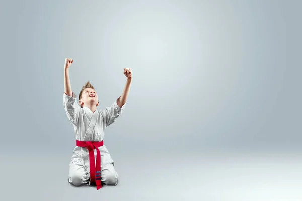 Creative background, a child in a white kimono rejoices victory, on a light background. The concept of martial arts, karate, sports since childhood, discipline, first place, victory. copy space.