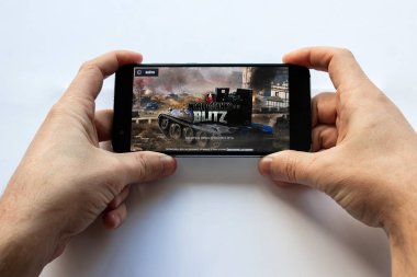Brest, Belarus, 22 Ocak 2019. Dünya Tanks oyunu ile akıllı telefon tutarak erkek eller. Tank oyun logo dünyası. Yumuşak odak.