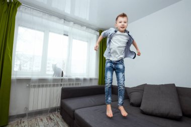 Çocuk oturma odasında kanepede atlar eğleniyor, çevresinde, ailesi evde olmadığı sırada dalga. Otururken, Bebek yalnız evde bebek.