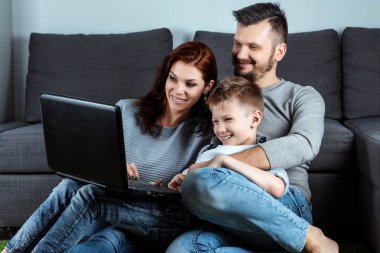 Mutlu bir aile ile bir laptop bir şey izlerken gülümsüyor. Ortak eğlence, tatil, ortak dinlenme, aile ilişkileri kavramı.