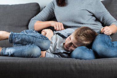 Çocuk annesi bir karın ağrısı ile kanepede yatıyor. Velayet, ebeveyn Bakımı, mide problemleri, gıda zehirlenmesi, çocuk sorunları kavramı.