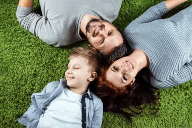 Üstten Görünüm, mutlu bir aile, baba anne ve oğlu yeşil bir halı üzerinde yalan gülümsüyorsun. Aile, aile ilişkileri, mutluluk, sevinç kavramı.