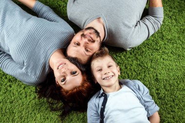 Üstten Görünüm, mutlu bir aile, baba anne ve oğlu yeşil bir halı üzerinde yalan gülümsüyorsun. Aile, aile ilişkileri, mutluluk, sevinç kavramı.