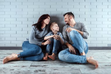 Mutlu bir aile gri duvara katta oturuyor. Evde oturan çift gülümsüyor. Uzay kopyalayın. Konut, kredi, mortgage bir aile kavramı.