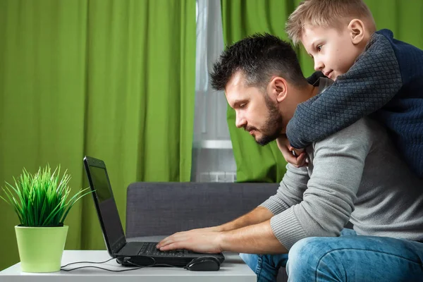 Father and son working on a laptop. Businessman working from home and looking after a child, spending time with a child. The concept of StartUp, Freelance, a successful modern family.