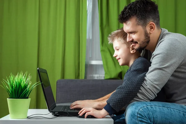 Father and son working on a laptop. Businessman working from home and looking after a child, spending time with a child. The concept of StartUp, Freelance, a successful modern family.