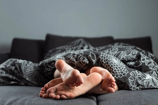 Las piernas, los pies de una pareja enamorada sobresalen de debajo de la manta. Día de San Valentín o historia de amor. Preludio en la cama, sexo, sitios para adultos, amor, relaciones . — Foto de Stock
