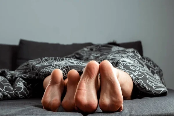 Beine, Füße eines verliebten Paares ragen unter der Decke hervor. Valentinstag oder Liebesgeschichte. Auftakt im Bett, Sex, Erwachsenen-Sites, Liebe, Beziehungen. — Stockfoto