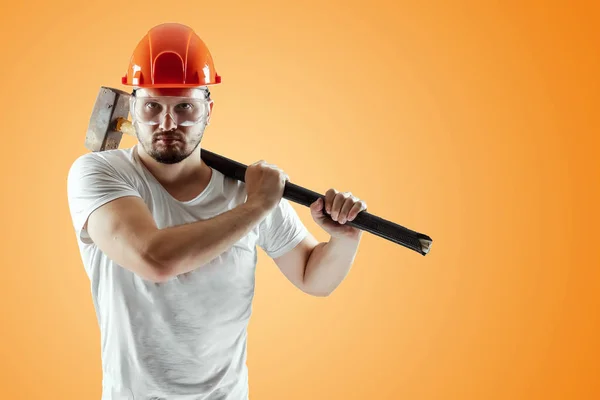 Бородатий чоловік у шоломі тримає санчата на помаранчевому тлі. Концепція будівництва, підрядник, ремонт . — стокове фото