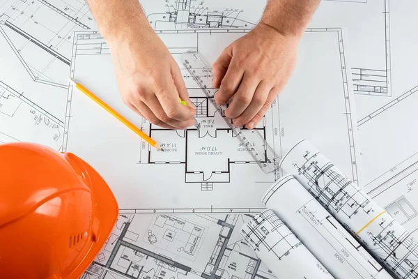 Мужские руки, оранжевый шлем, карандаш, архитектурные чертежи, рулетка. Архитектор проектирует здание. Концепция архитектуры, строительства, инжиниринга, дизайна. Копирование пространства . — стоковое фото