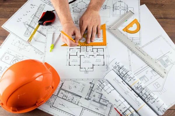 Manos masculinas, casco naranja, lápiz, dibujos de construcción arquitectónica, cinta métrica. El arquitecto diseña el edificio. El concepto de arquitectura, construcción, ingeniería, diseño. Copiar espacio . —  Fotos de Stock