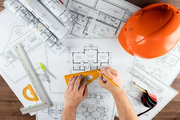 Мужские руки, оранжевый шлем, карандаш, архитектурные чертежи, рулетка. Архитектор проектирует здание. Концепция архитектуры, строительства, инжиниринга, дизайна. Копирование пространства . — стоковое фото
