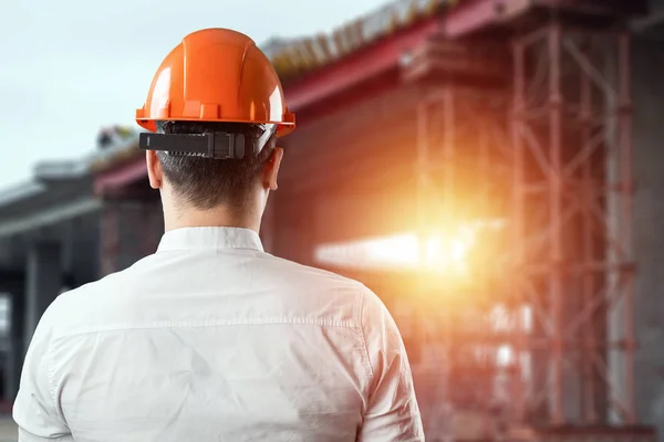 Портрет мужчины сзади в конструкции, оранжевый шлем на фоне строительной площадки. Концепция архитектуры, строительства, проектирования, проектирования, ремонта. Копирование пространства — стоковое фото