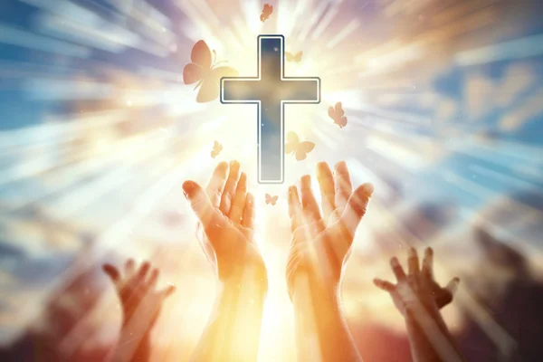 Těsné ruce na pozadí symbolu křesťanské, modlitební, katolického kříže, hejna motýlů. Křesťanské náboženství, pojetí naděje, víry, náboženství, symbol naděje a freedo — Stock fotografie