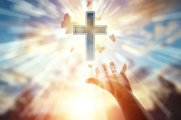キリスト教、祈り、カトリックの十字架、蝶の群れのシンボルの背景にクローズアップ手。キリスト教、希望、信仰、宗教、希望と自由の象徴の概念 — ストック写真