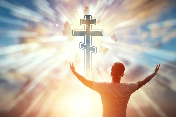 Mann auf dem Hintergrund des Symbols des Christentums, Gebet, orthodoxes Kreuz auf dem Hintergrund des Sonnenuntergangs. das Konzept der Hoffnung, des Glaubens, der Religion, ein Symbol der Freiheit. — Stockfoto