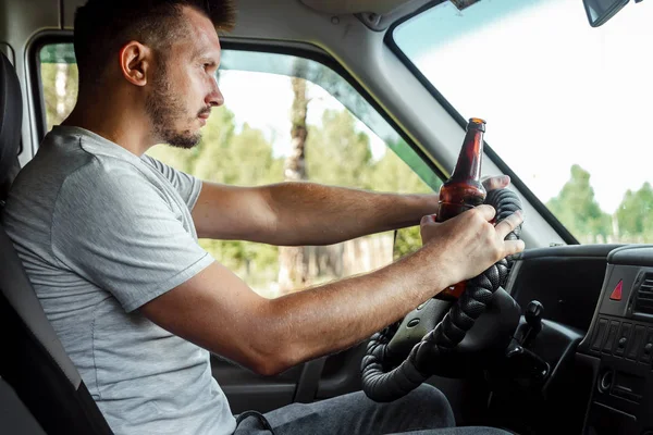 Muž u volantu drží v ruce láhev alkoholu, porušuje dopravní pravidla. Koncept nehody, narušení provozu — Stock fotografie