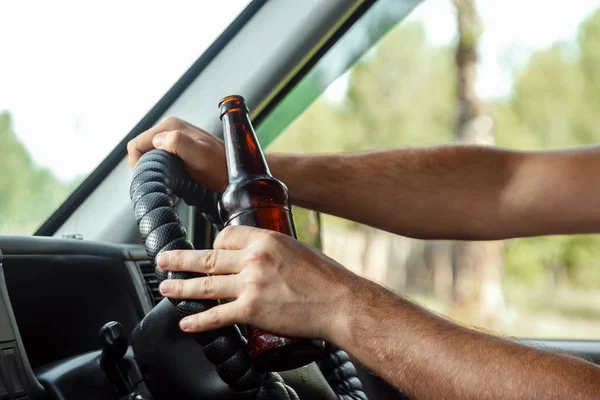Muž u volantu drží v ruce láhev alkoholu, porušuje dopravní pravidla. Koncept nehody, narušení provozu — Stock fotografie