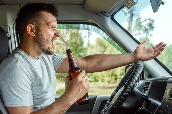 A man at the wheel holds a bottle of alcohol in his hand while driving, violates traffic rules. The concept of an accident, a traffic violation